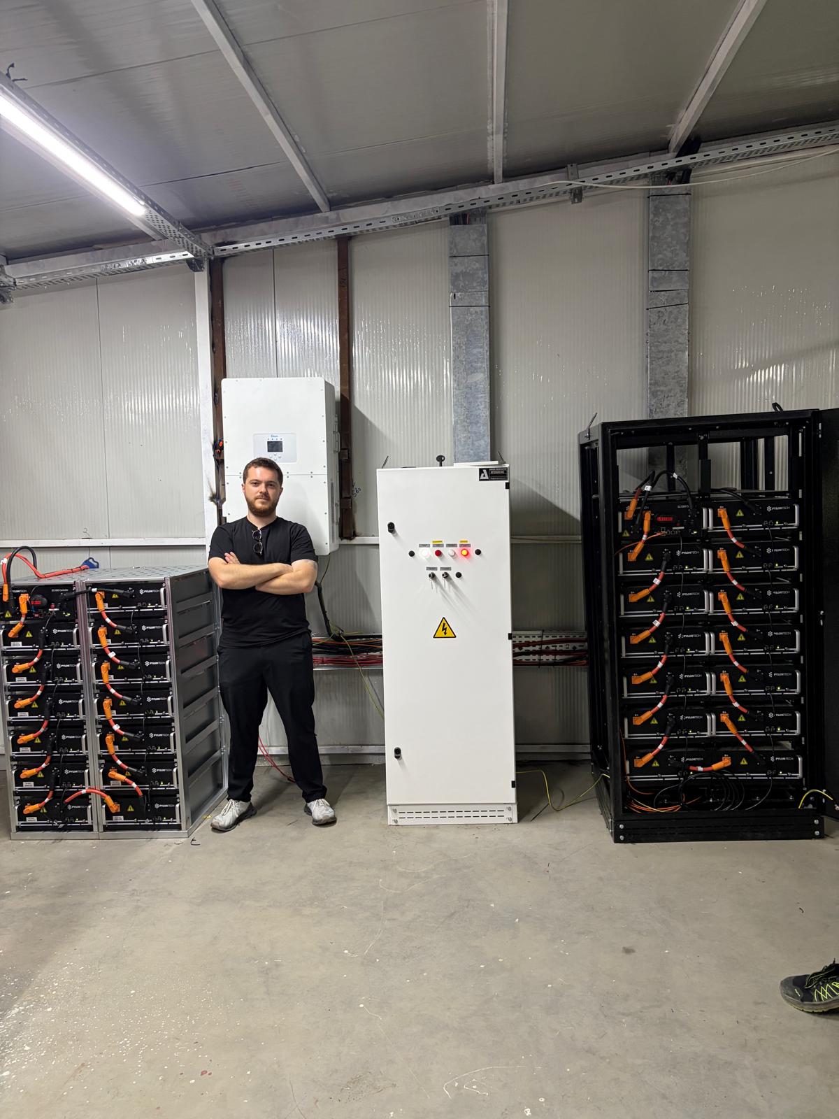 Berk Akgül, endüstriyel batarya kabinleri ve elektrik panosunun yanında